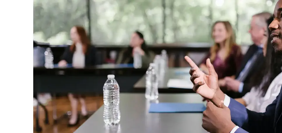 Meeting takes place in a large room, with many seated delegates round the table, with the closest gesturesg while he makes his point